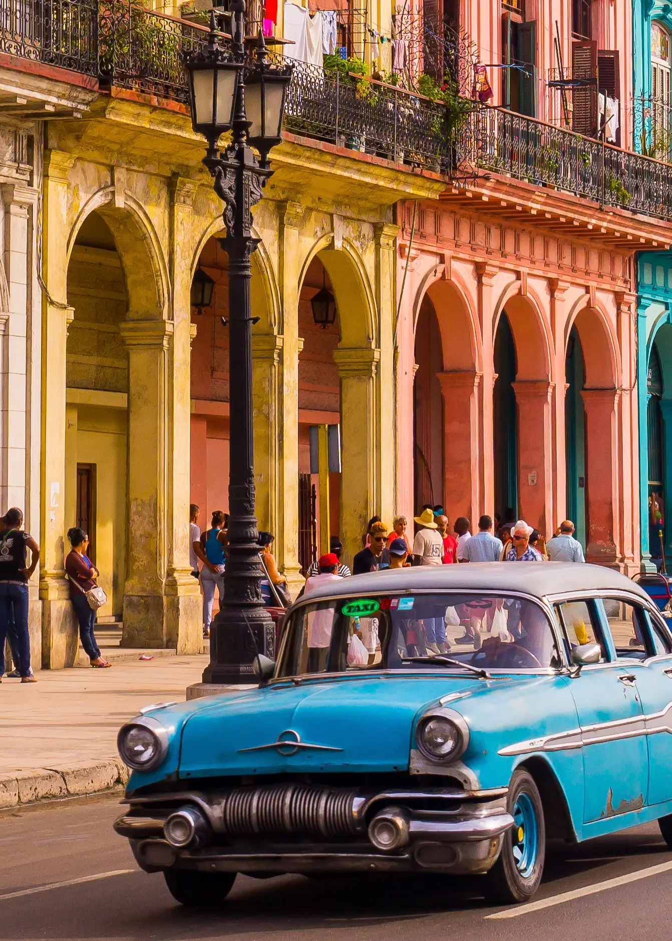 A blue oldtimer taxi is driving through Habana Vieja in front of a colorful façade.