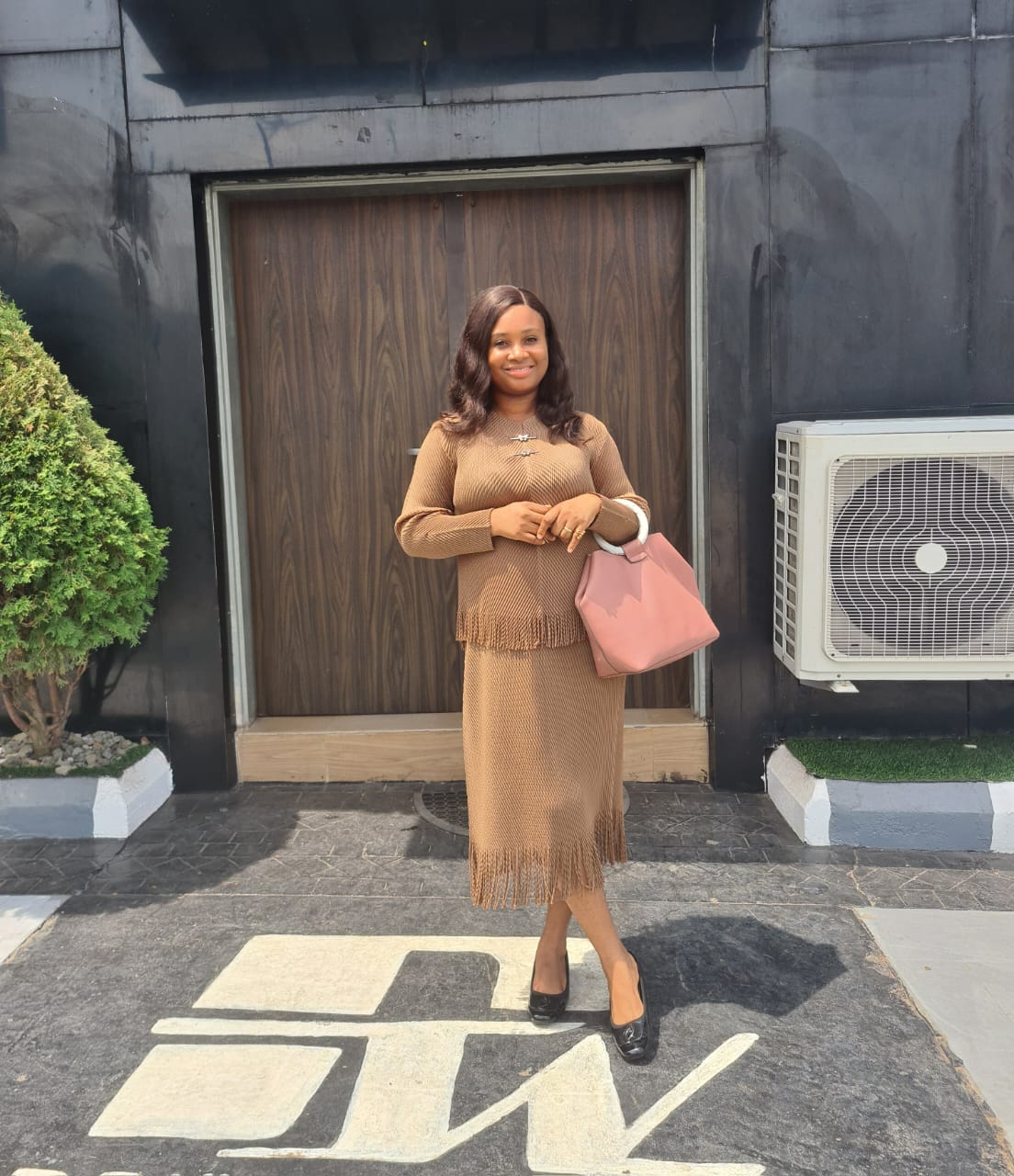 Goodluck Ndubuisi stood outside in a brown outfit holding a handbag