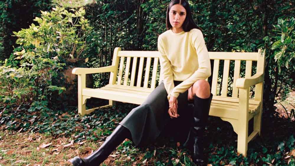 Emma sitting on a garden bench surrounded by green plants and shrubs.