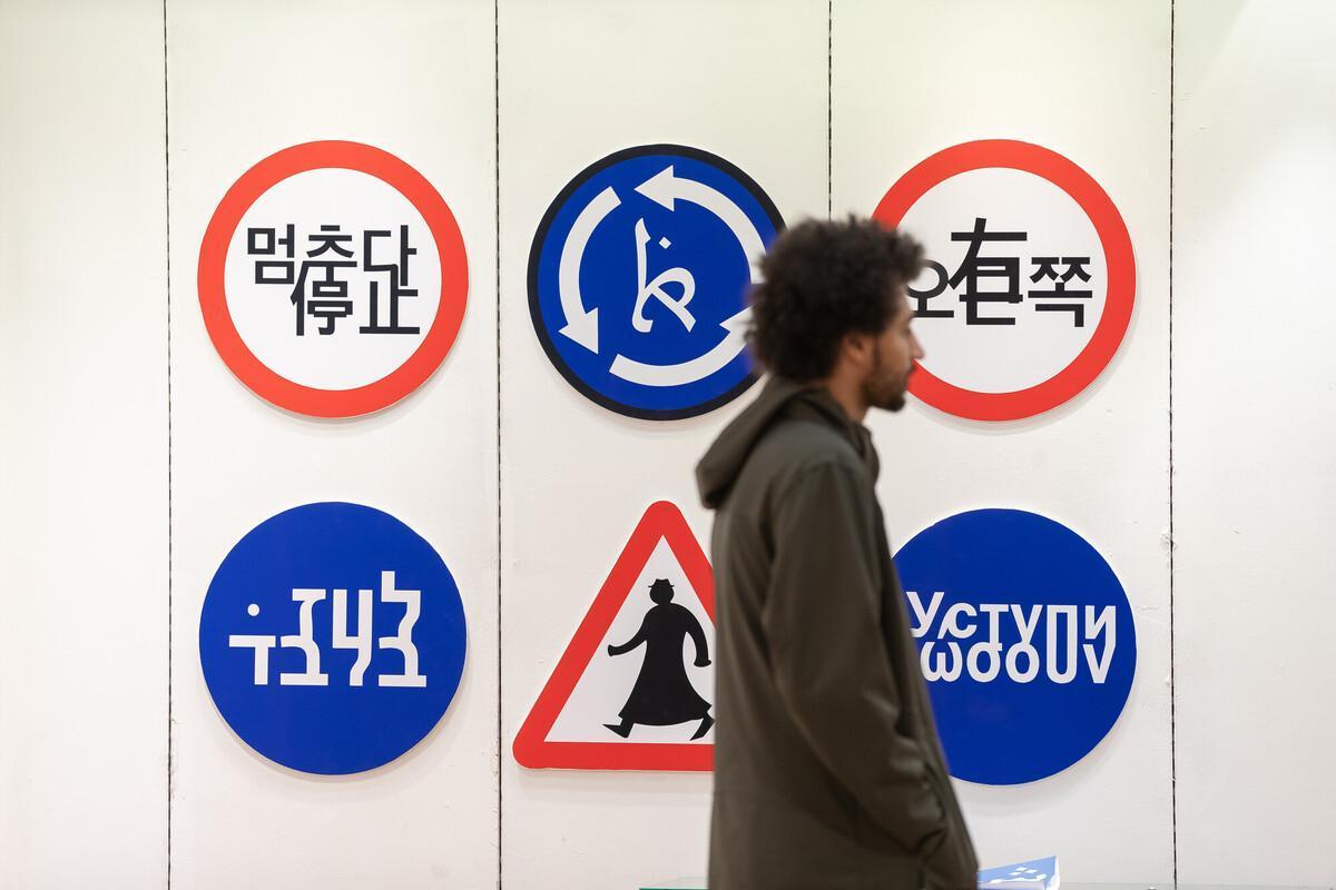 Graphic Design BA (Hons) exhibition with creative road sign designs and a student walking past the display.