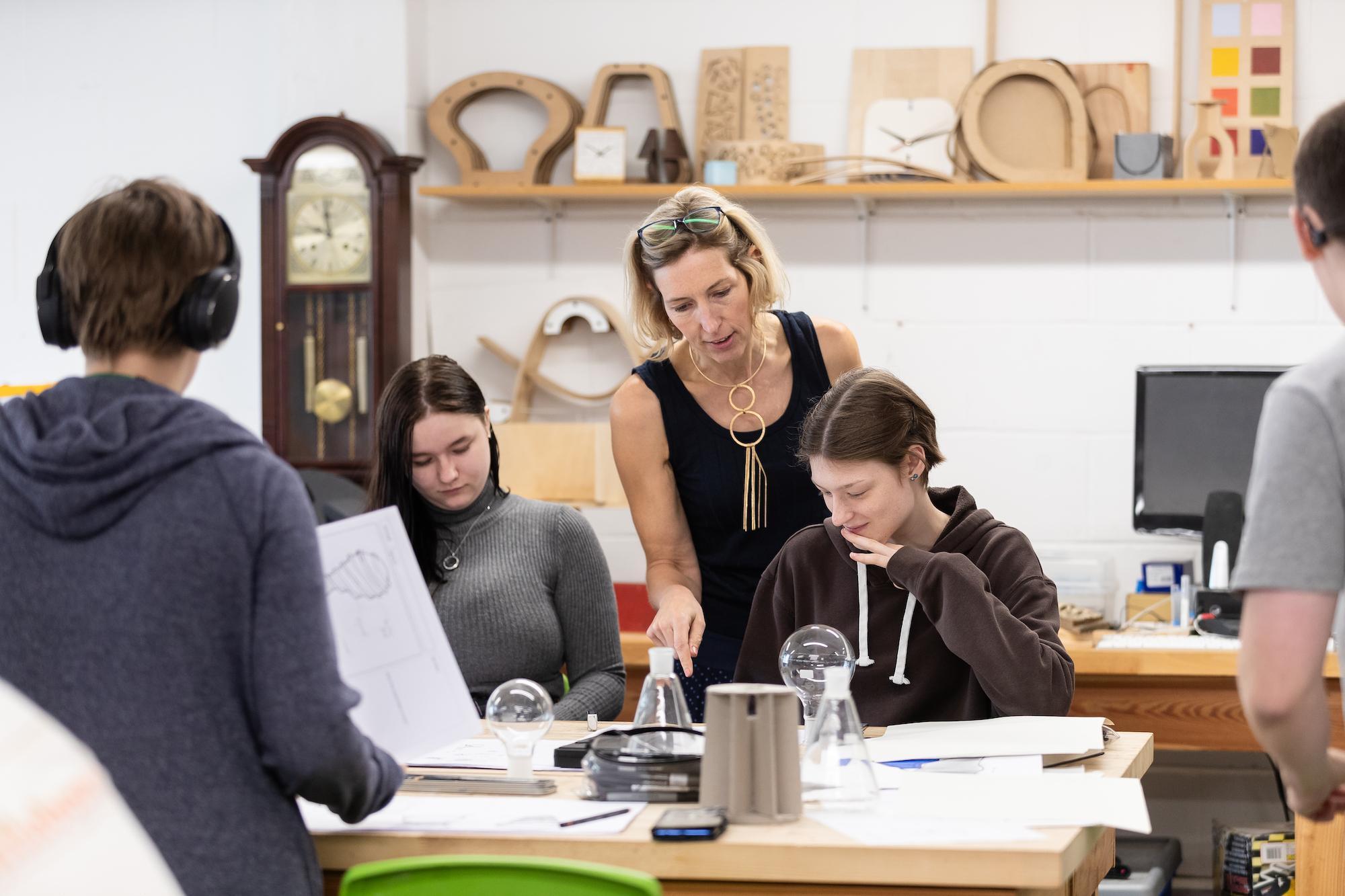 Product Design BA (Hons) students working on creative prototypes with guidance from a lecturer in a university design studio, developing innovation and technical design skills.