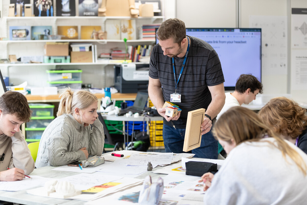 A group of students with a tutor in a art class working with art design materials.