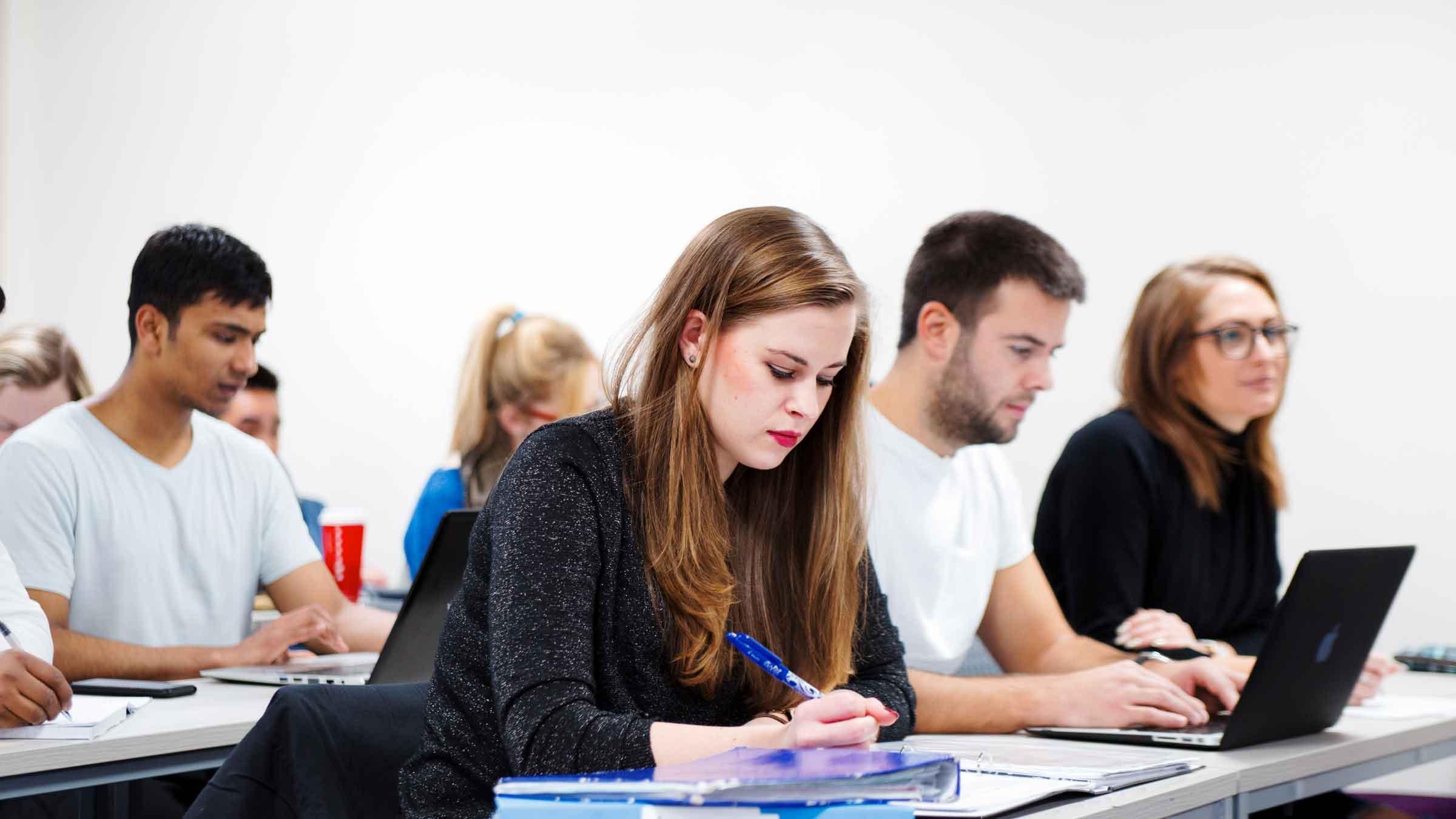 Postgraduate Accounting MSc students working in a modern classroom, taking notes and using laptops during an advanced accounting seminar