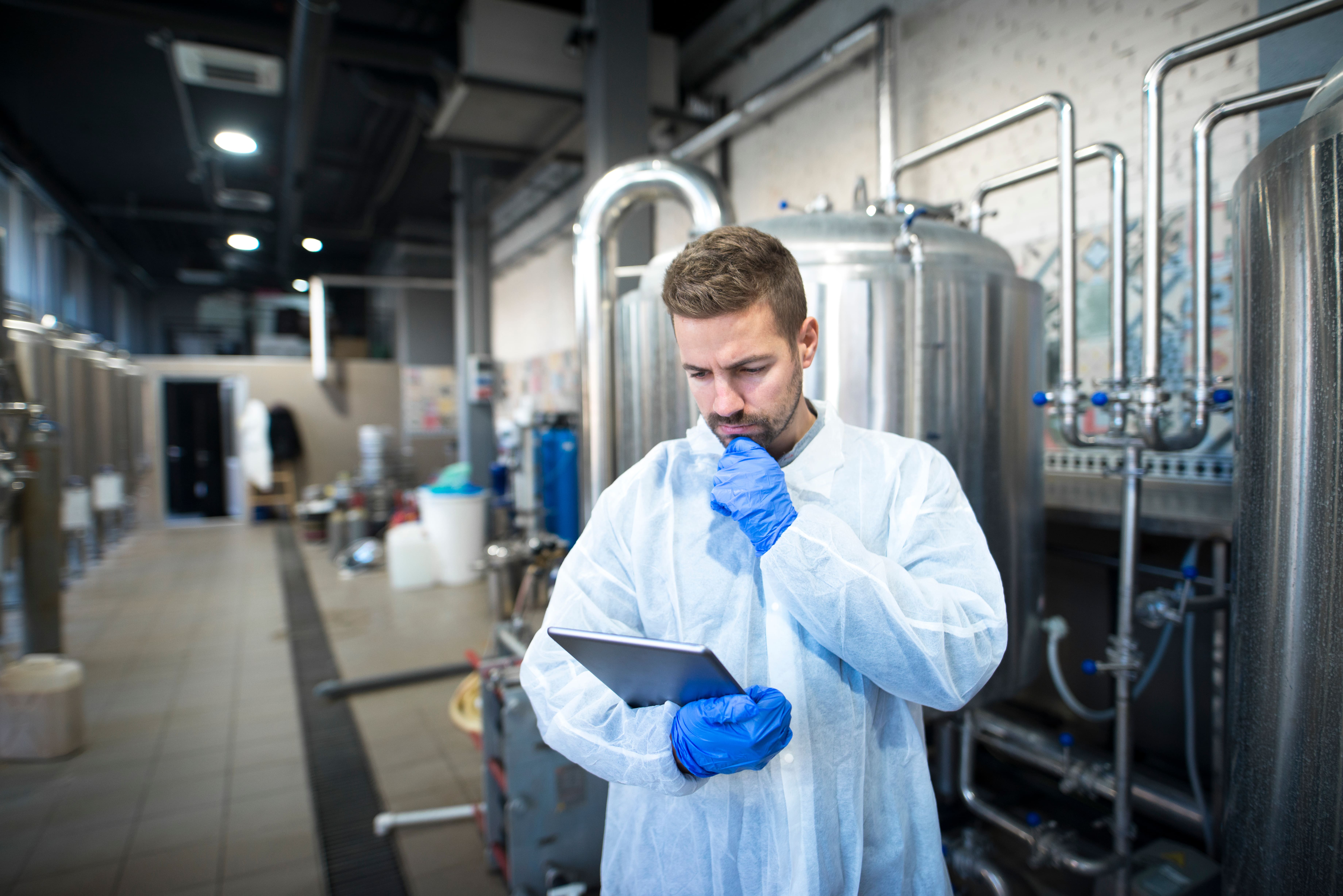 Technologist reading production reports on tablet computer in factory.