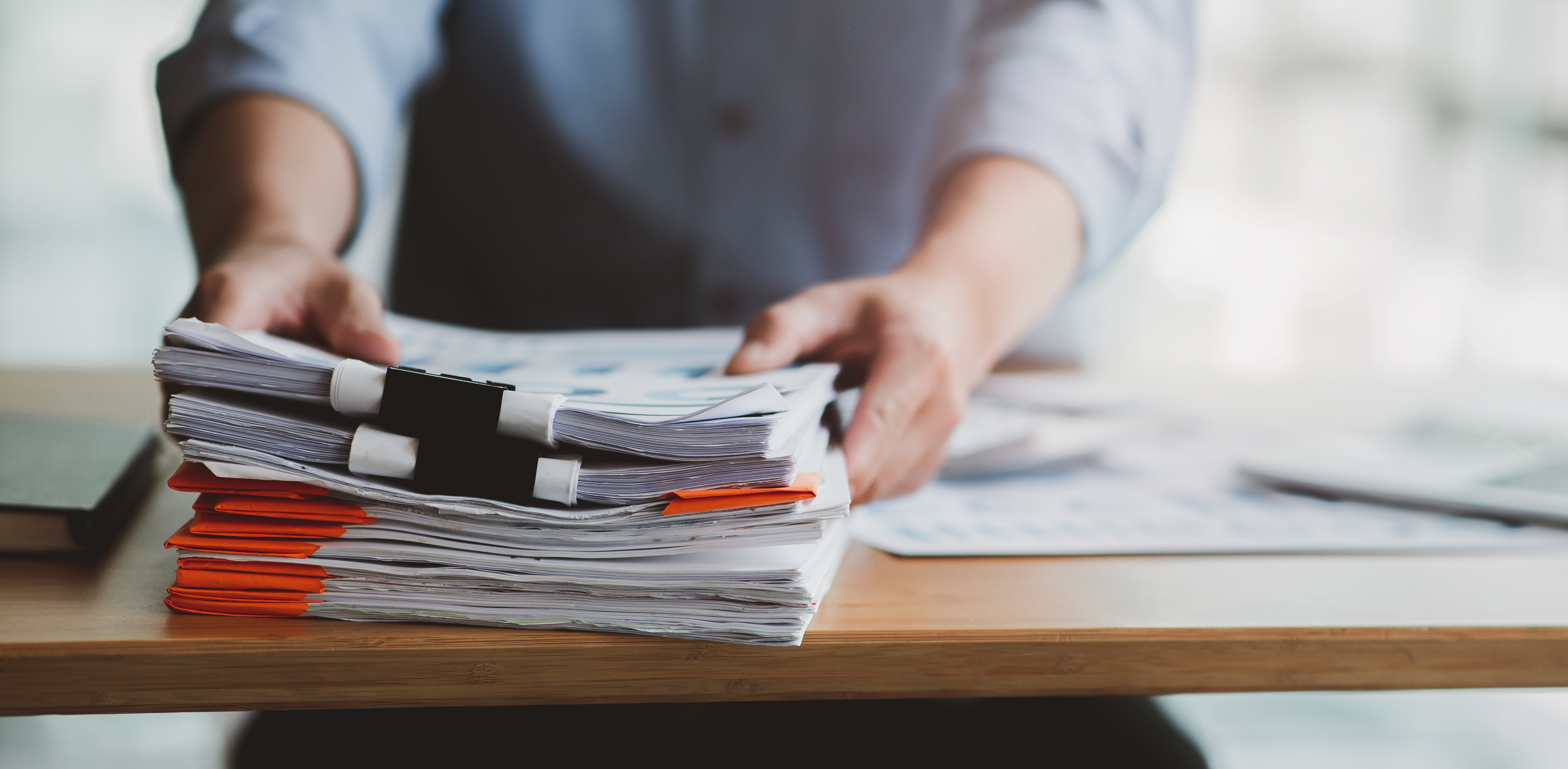 close up of a pile of documents with a person reaching out to pick them up off a table