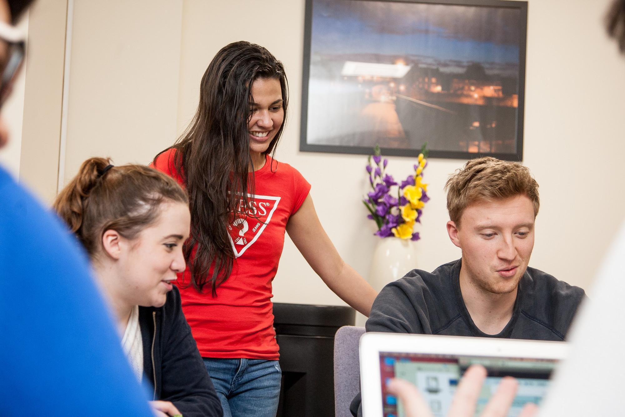 Three students collaborating around a laptop in a modern study space, discussing digital marketing strategies and analytics. The scene conveys teamwork, problem‑solving, and real‑world digital marketing practice, reflecting skills in SEO, content creation, data analysis, and campaign planning.