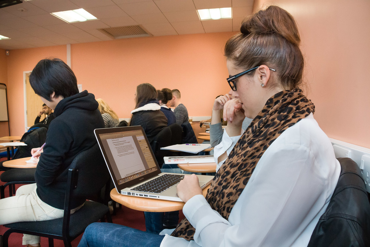 A student looking at her laptop and sitting in a lecture room with other students.