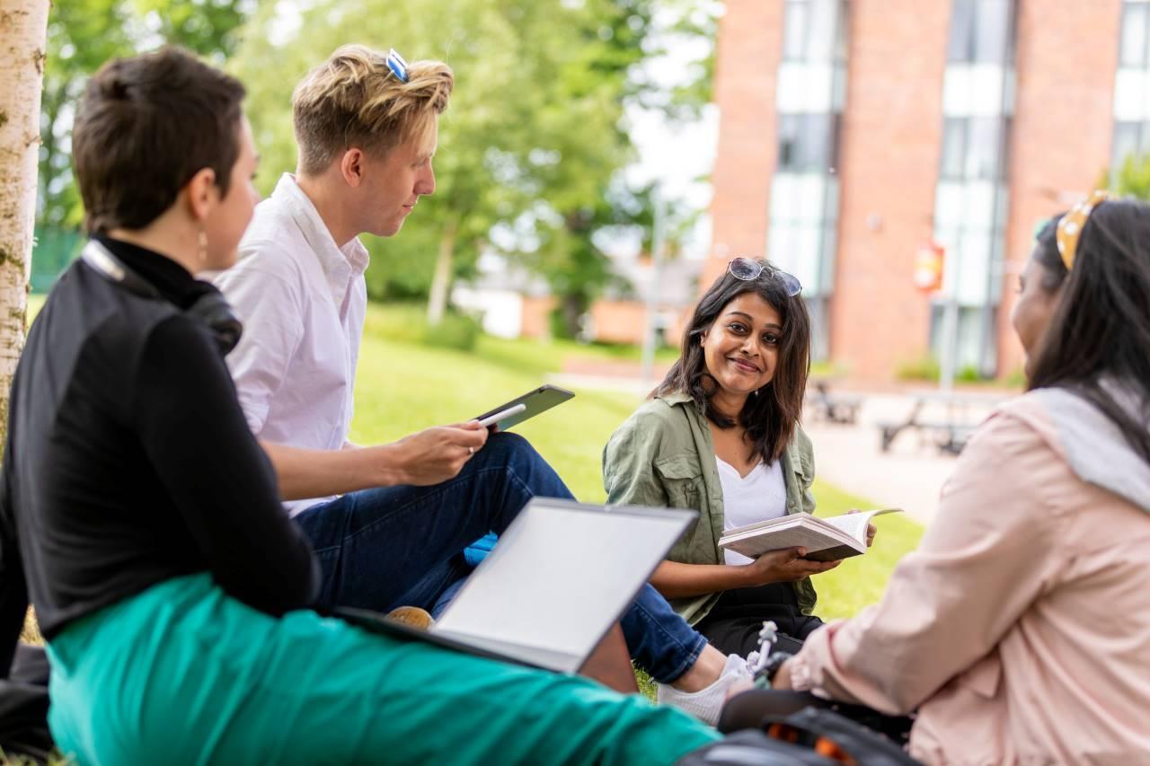 Students studying together outdoors on campus, using books and laptops, representing collaboration, communication, and international focus for Business Management and Spanish BA Hons.