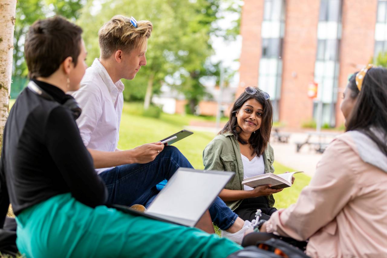 Business Management and Spanish BA (Hons) students studying outdoors with notebooks and laptops.