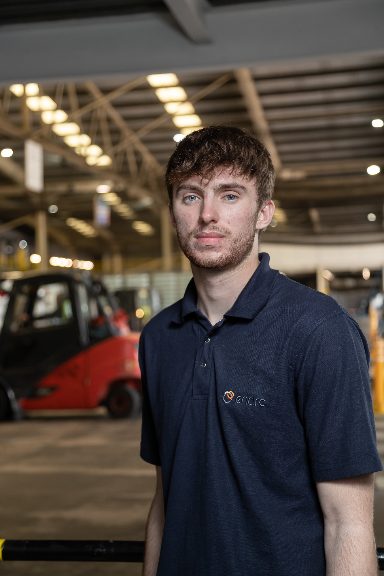 A male student on work based learning experience, looking forward in a warehouse with lifting equipment in background.