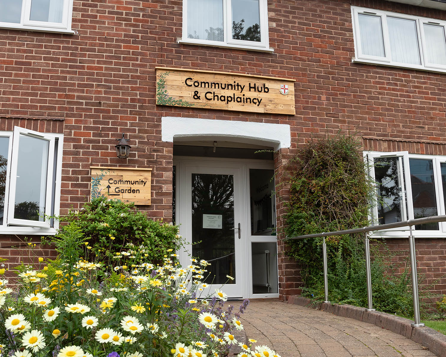 Welcoming entrance to the Chaplaincy Community Hub with garden signage and blooming flowers.