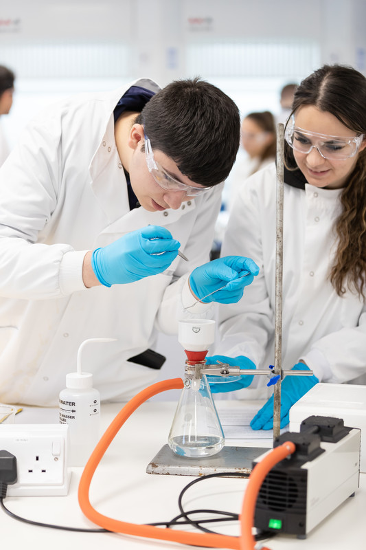 Chemistry students doing an expereiment in a lab wearing lab coats and glasses