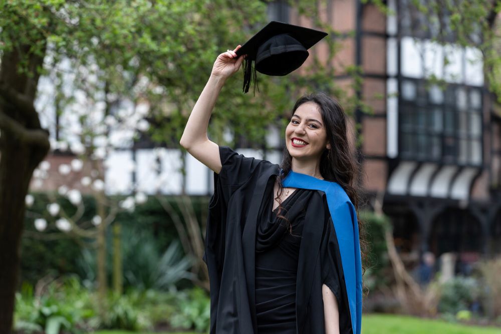 Mahshid standing outdoors lifting her graduation cap