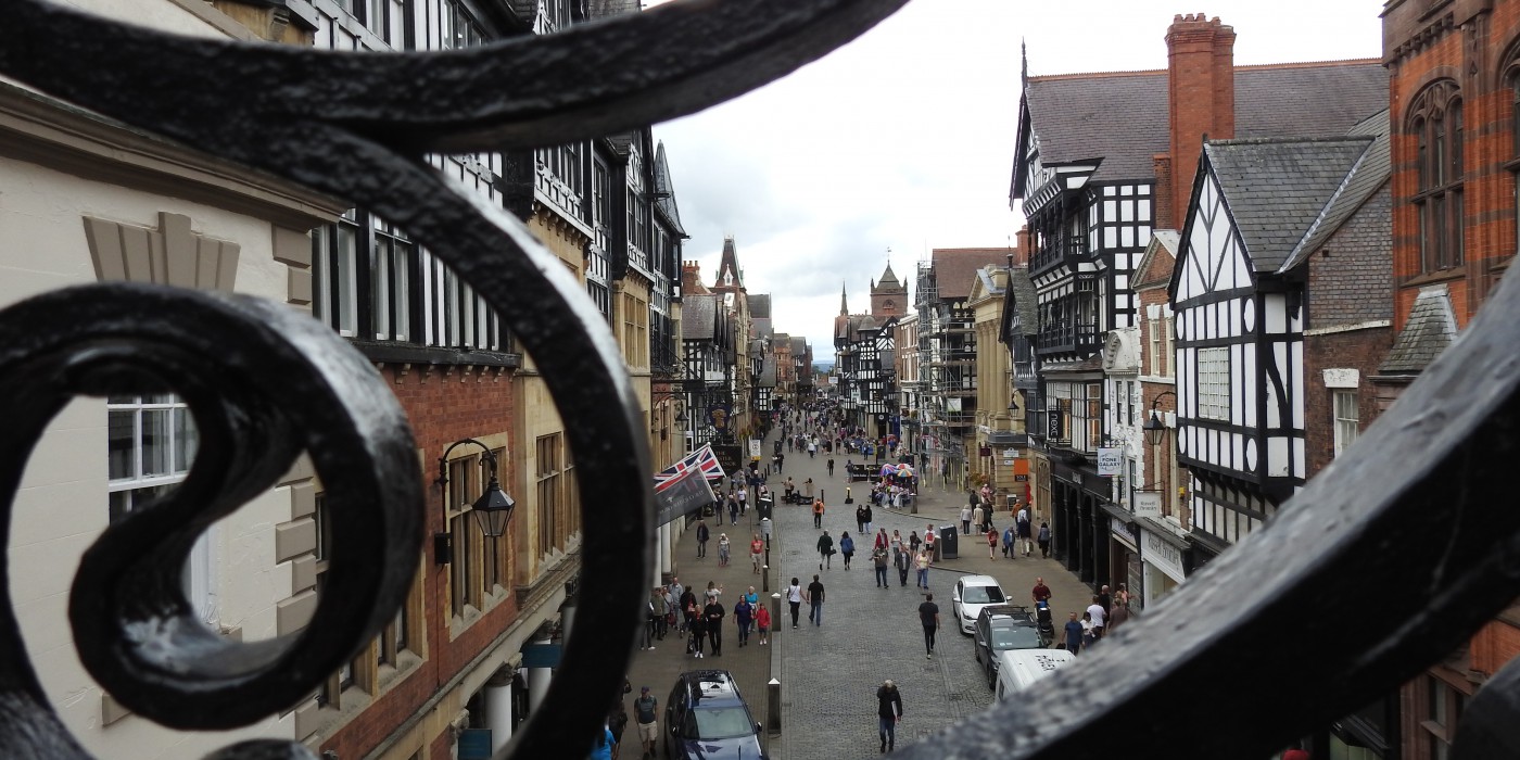 A birds eye view of Chester Foregate St, looking from the clock towards Watergate St, various shops and people are walking.
