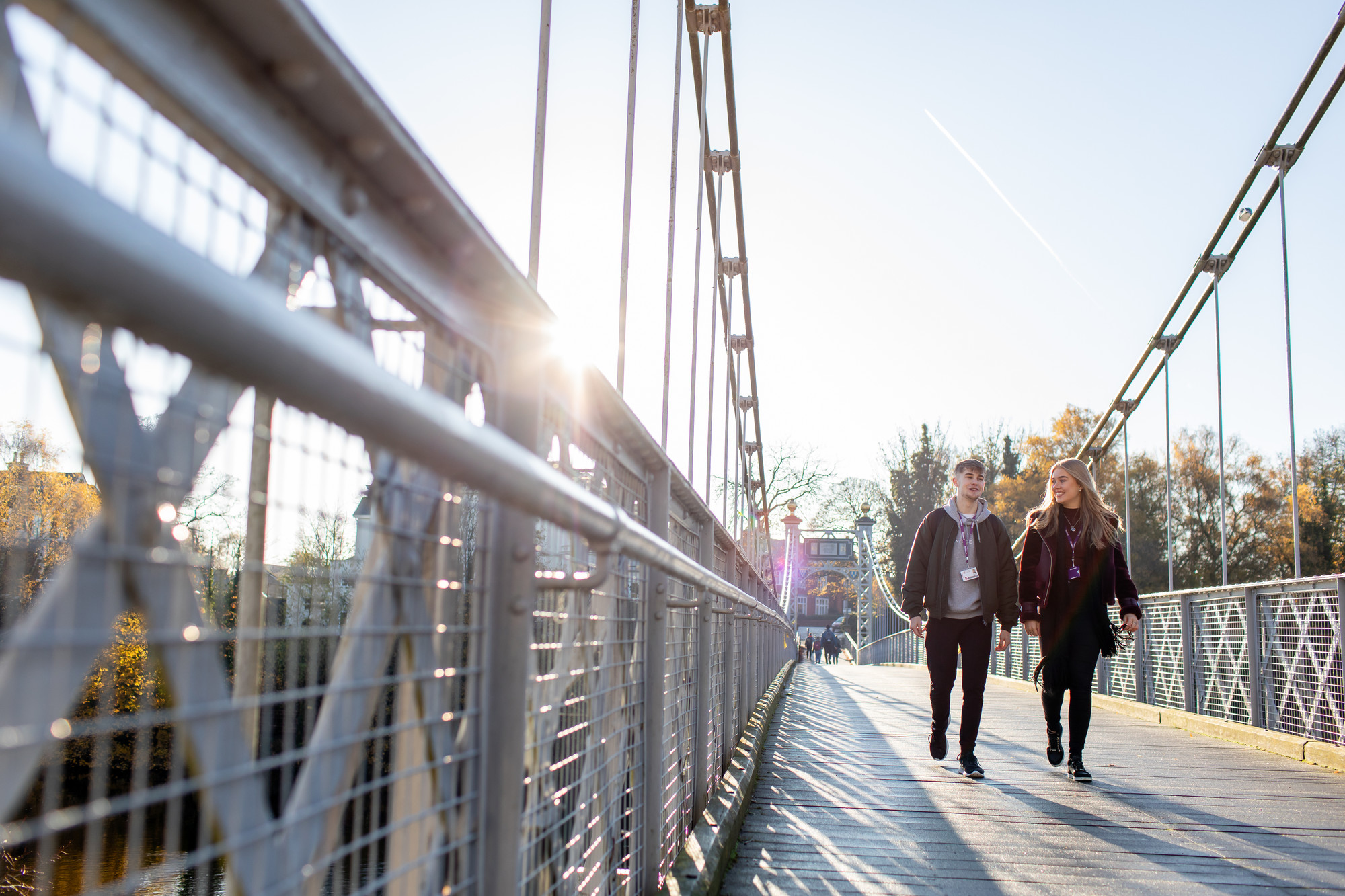A male and female student walking across Queens Park Bridge in sunny weather