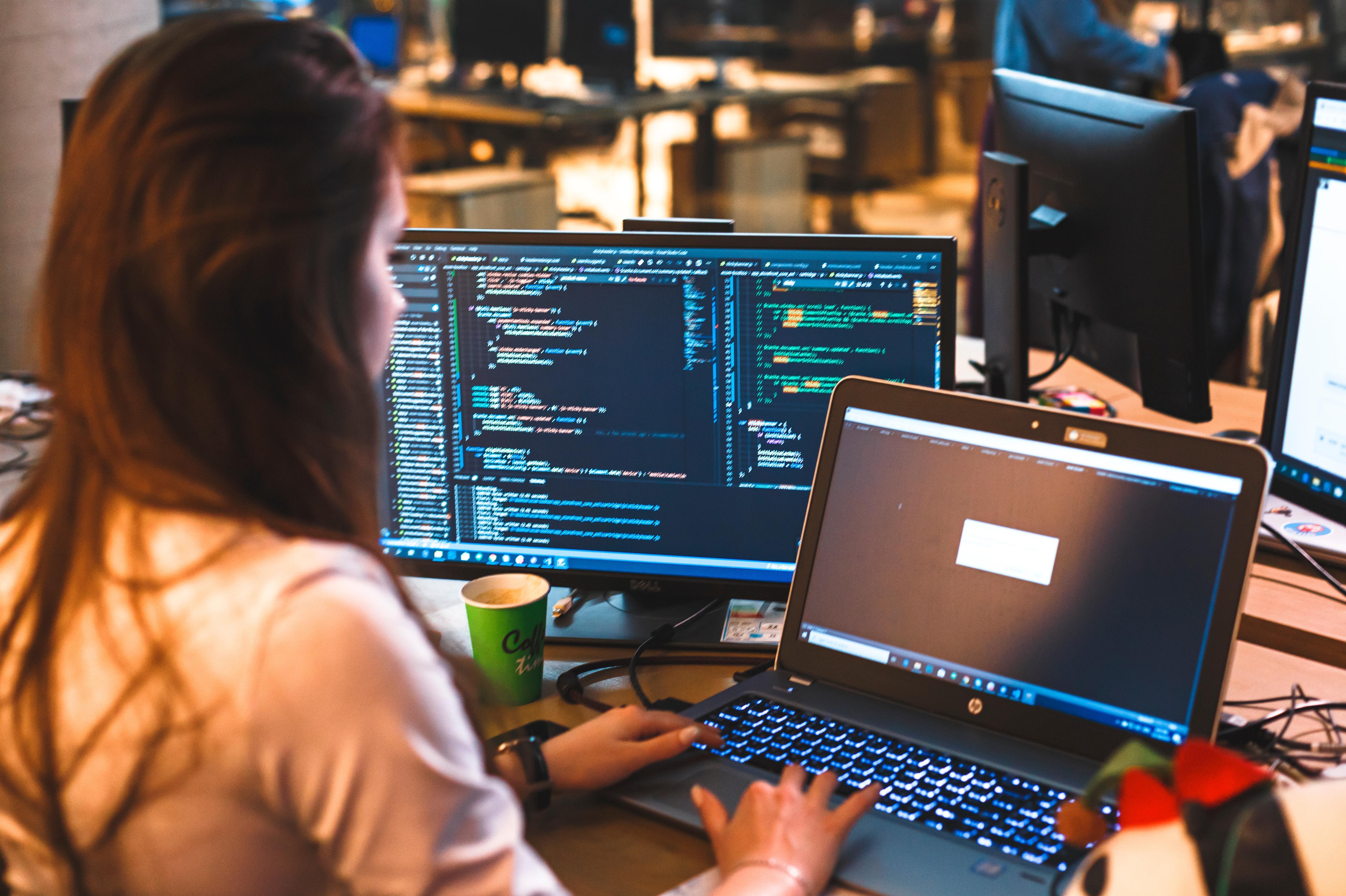Student working on laptop and dual monitors with code and machine learning models, demonstrating data analysis, programming and software development skills for Applied Artificial Intelligence MSc.