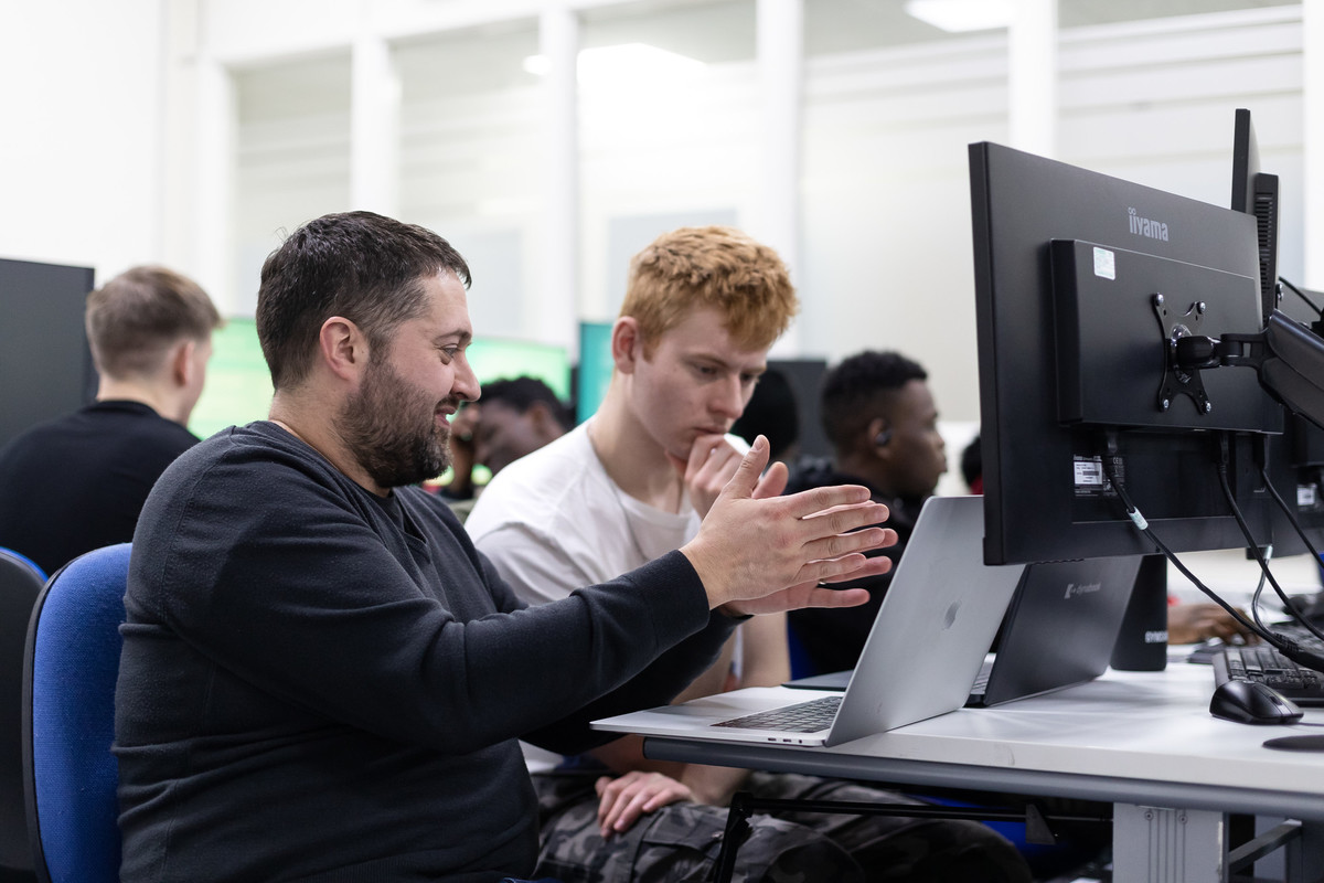 computing students sitting in forun of a pc in a classrooom