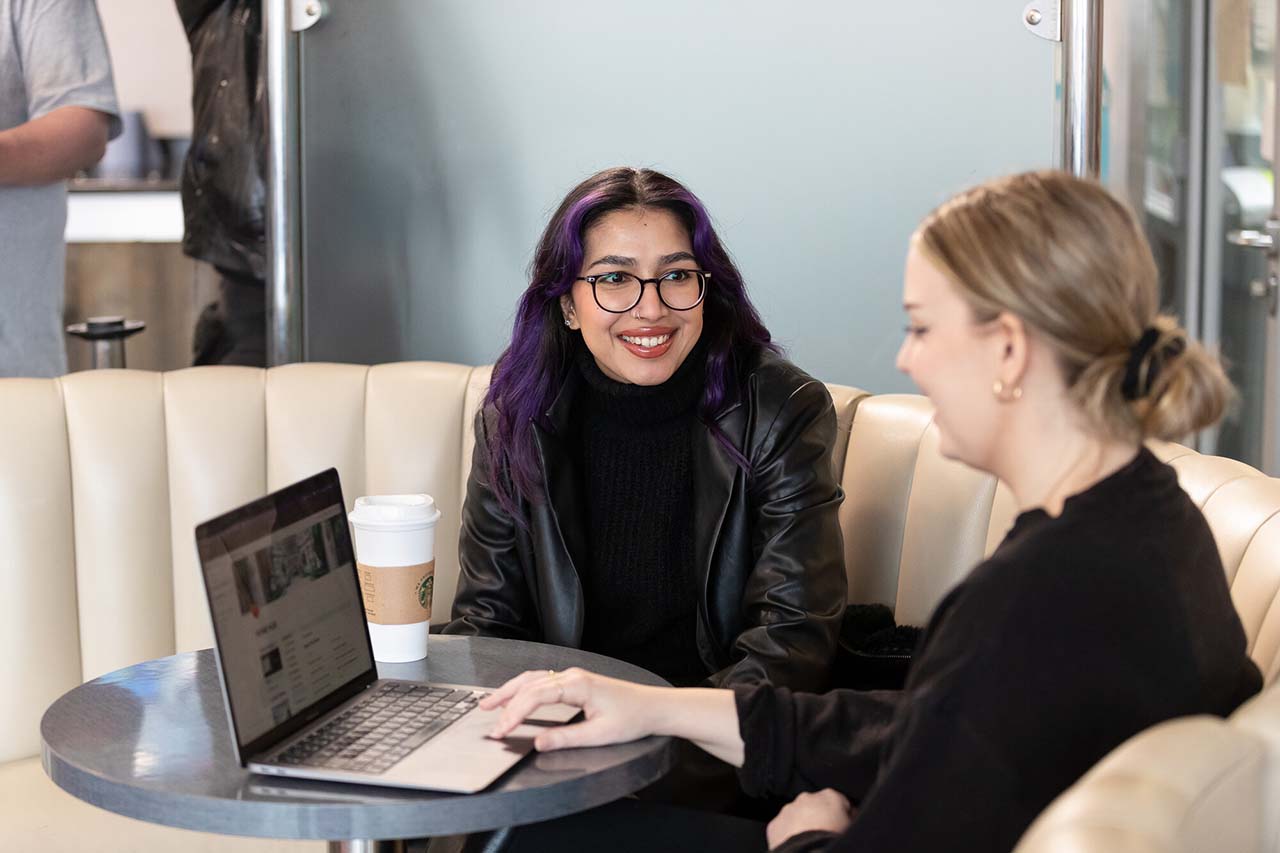 Two female students smiling while sitting at table with laptop screen open