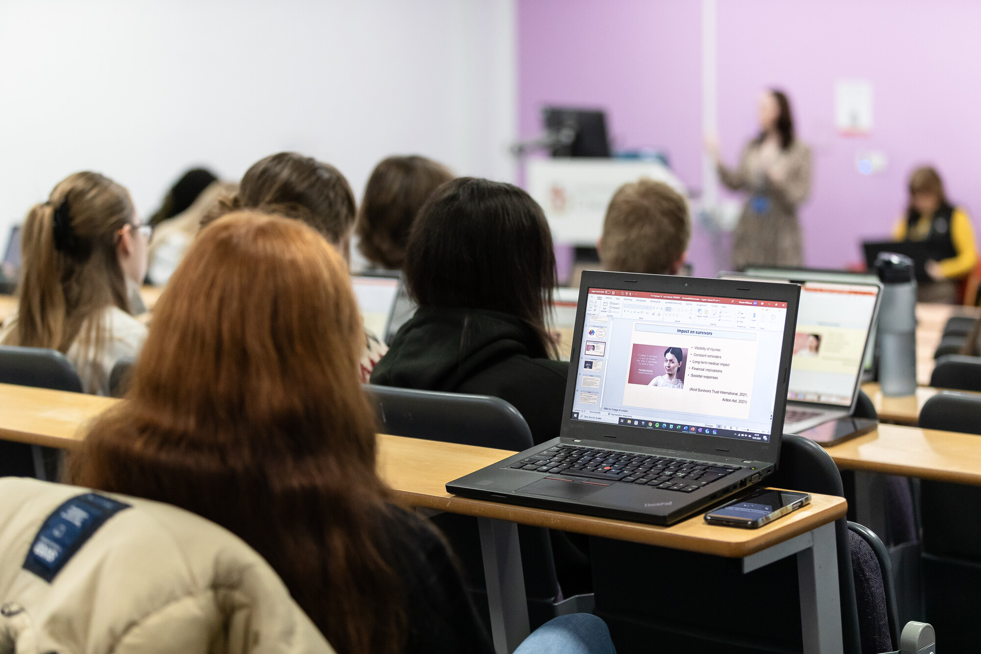 A group of students sitting in a lecture room, looking at laptop screens.