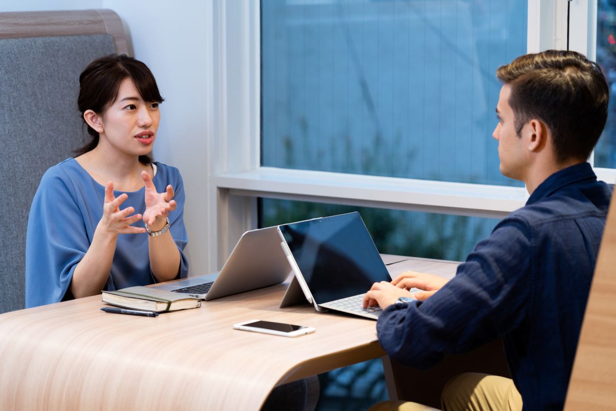 Two people sat at a desk with laptops having a discussion