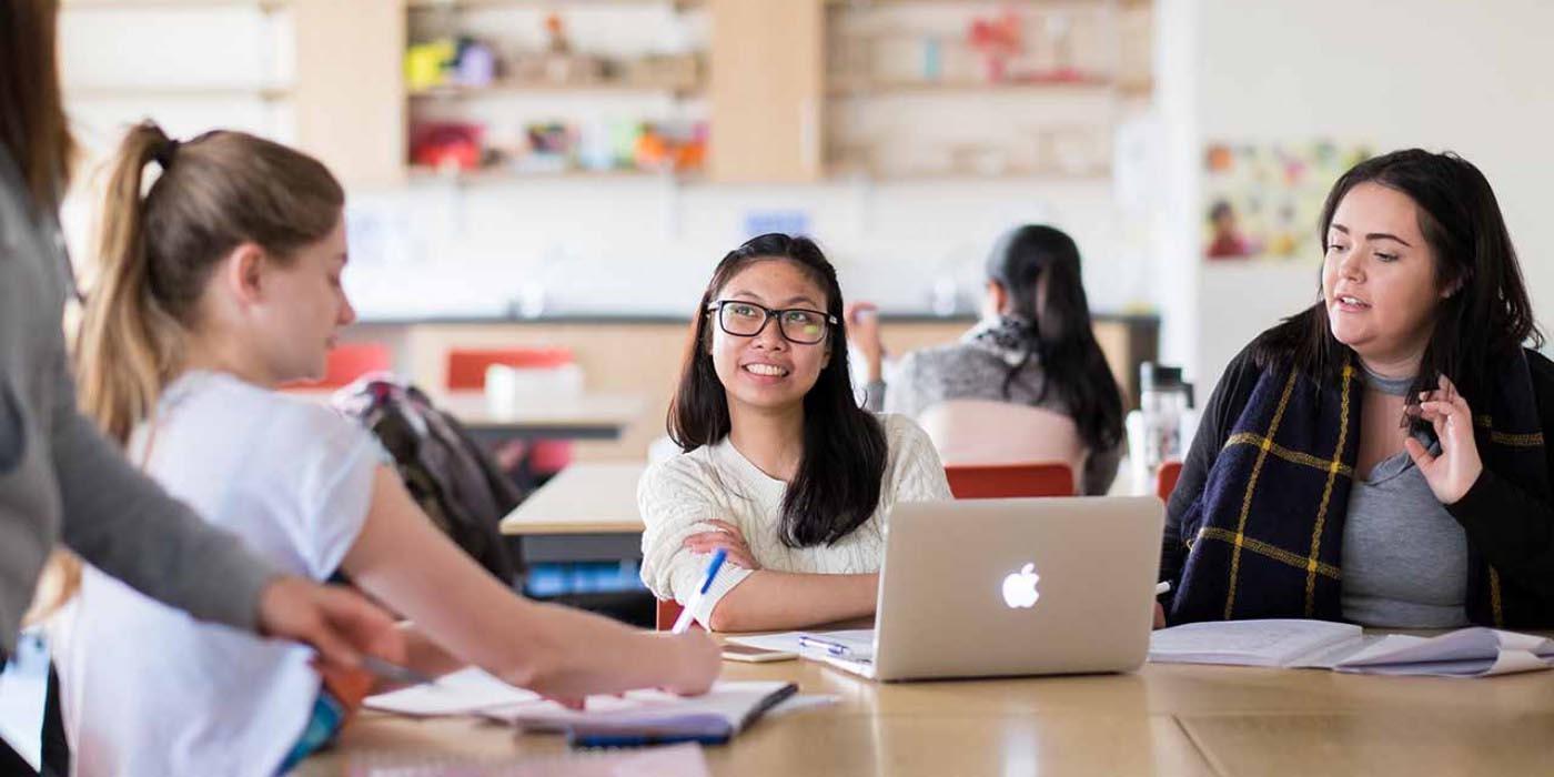 Trainee teachers collaborate in a classroom discussion using laptops and study materials, developing teaching expertise, subject knowledge and classroom practice for the Secondary Drama (School-Led) PGCE with QTS at the University of Chester.