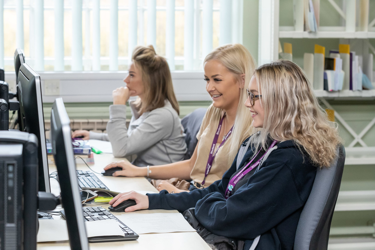 Three students working on desktop computers in a library.