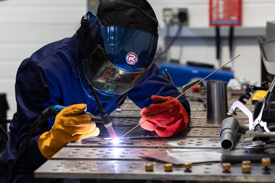 A man in protective screen using a welding tool in mechanical engineering workshop.