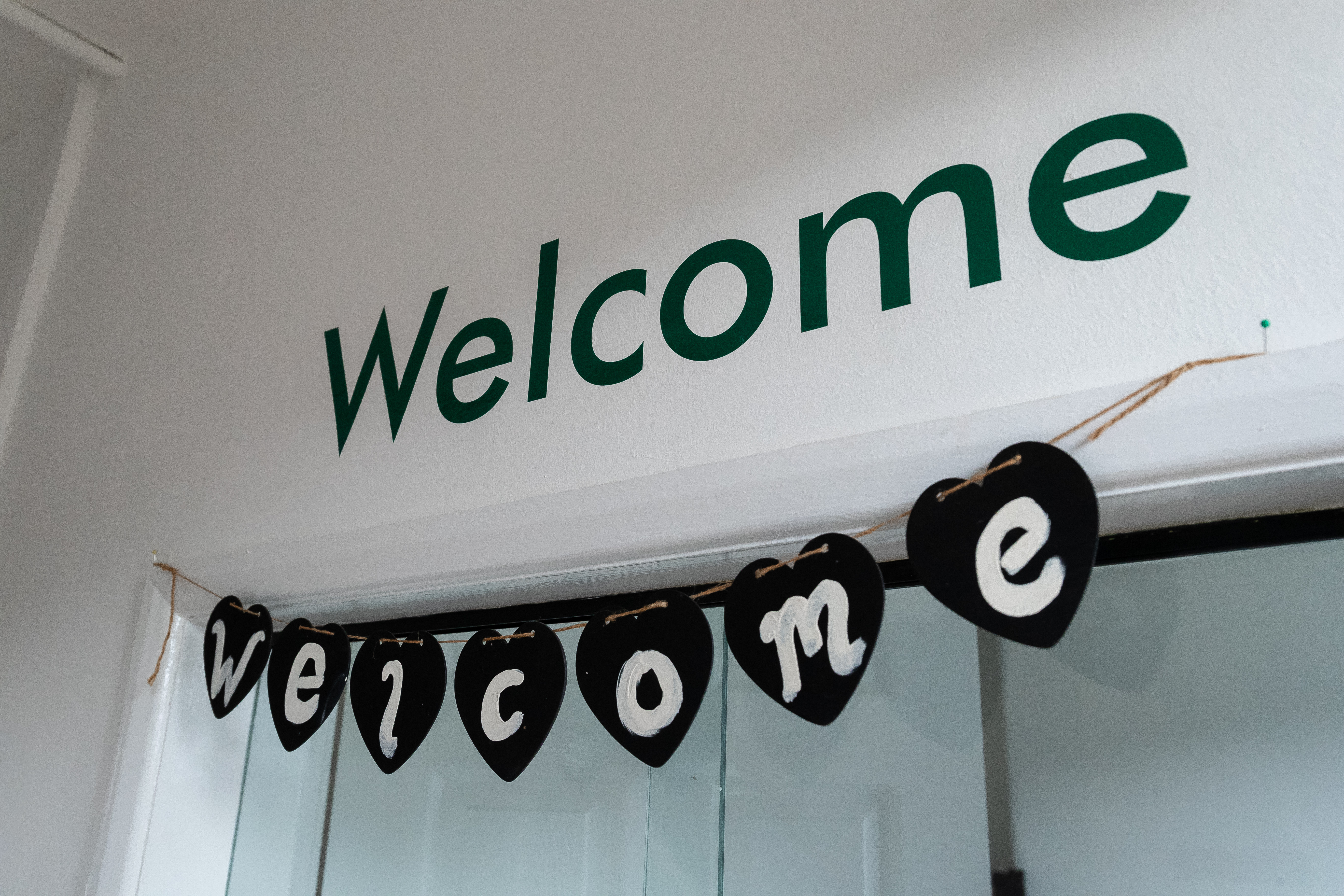 Green “Welcome” lettering on a white wall above a handmade welcome bunting hanging across a doorway.