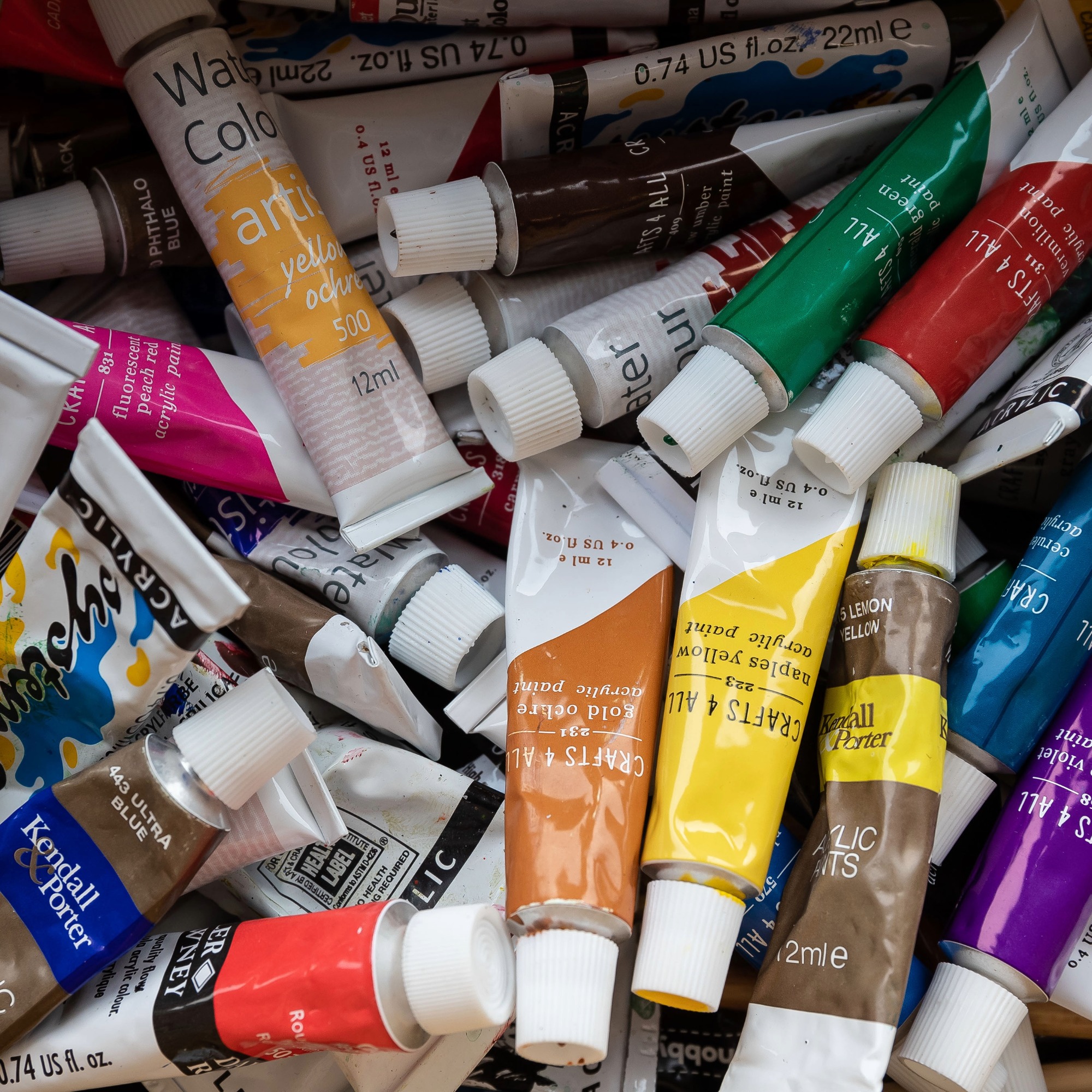 A collection of colourful acrylic paint tubes arranged together, including shades of yellow, blue, red, green, orange and purple.