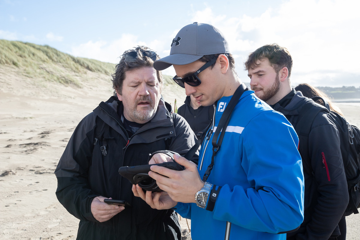 Three people standing outdoors looking at object found on a beach.