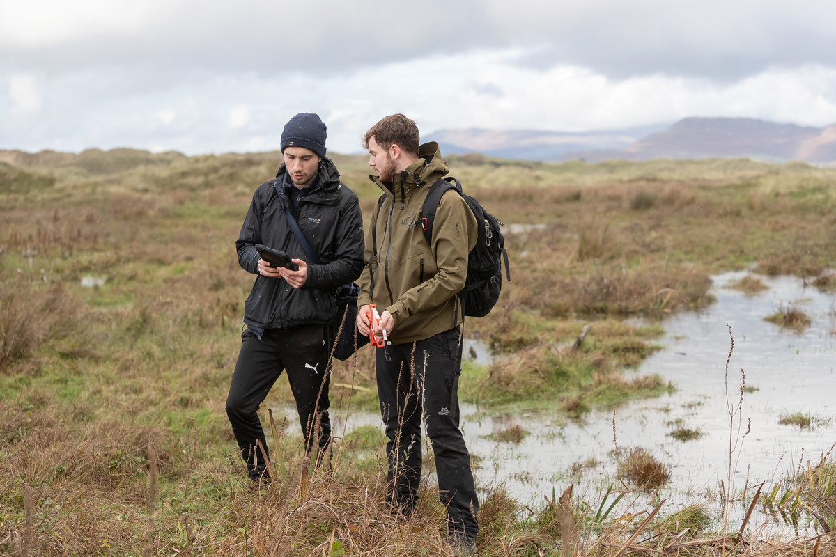 Two people walking outdoors in an hill landscape.