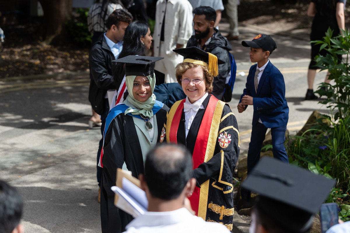 A person in graduation clothing stands with the VC