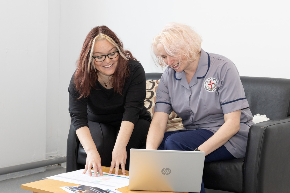 Two people sat at a desk using a laptop and reading papers