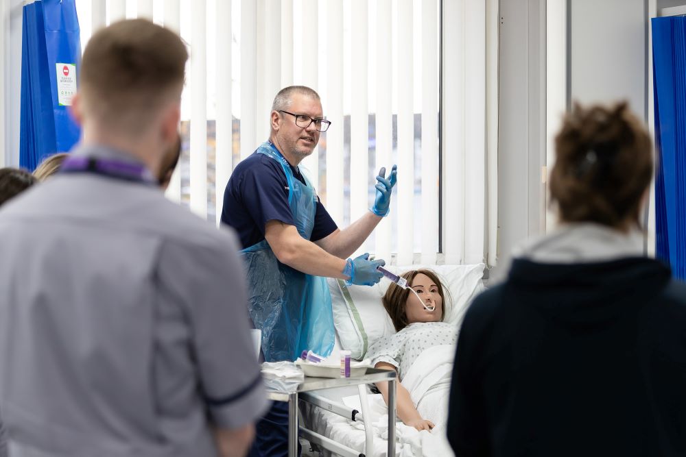 Tutor in a nursing simulation suite demonstrating to students how to use equipment during a skills lab session