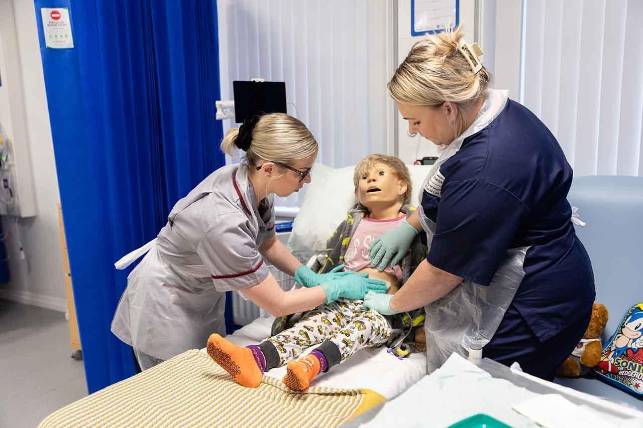 Nursing associate students practice clinical skills on a child medical training mannequin during a simulation session as part of the Nursing Associate Higher Apprenticeship FdSc programme.