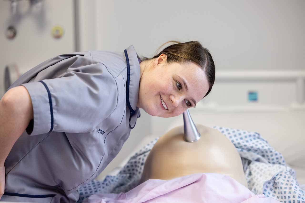 A nurse listening for baby heart beat on ward simulation midwifery training session.