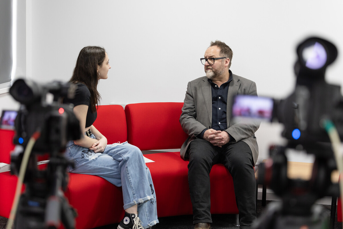 Interview setting on a red sofa with cameras and microphones