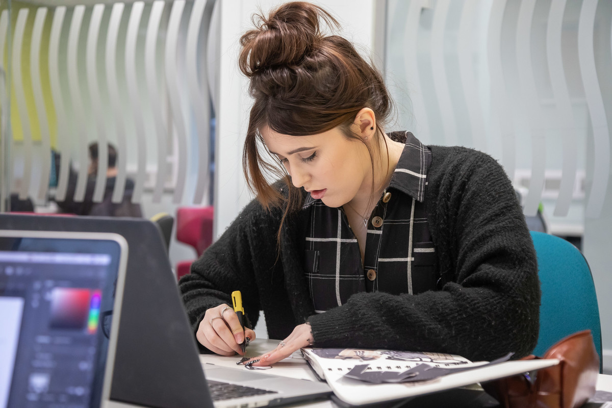 A student studying at a desk in a room with desk top computer and notebooks.