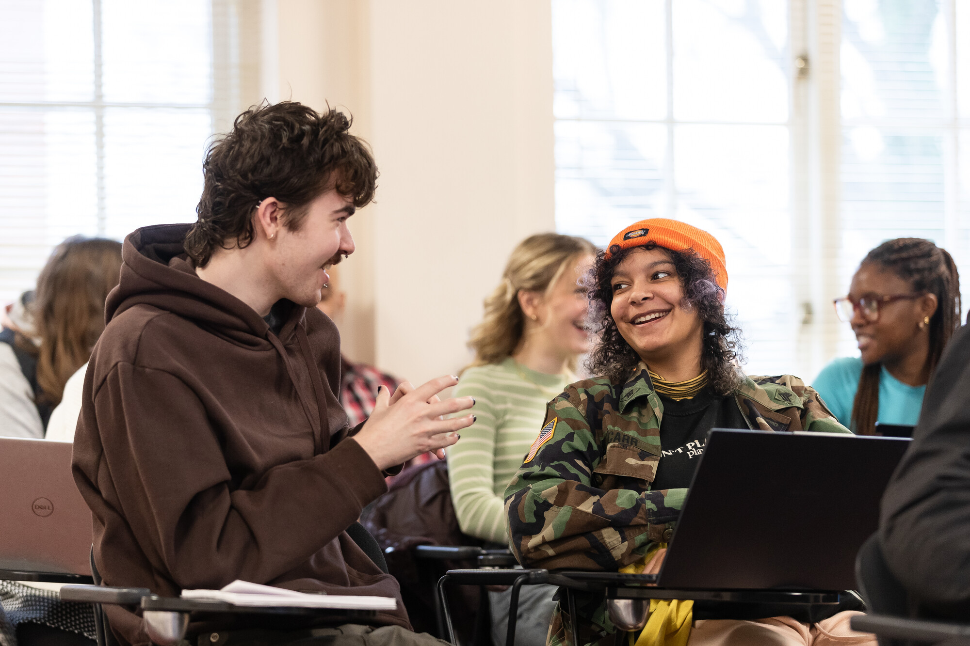 two Students talking, smiling and engaged in a conversation sitting in a classroom