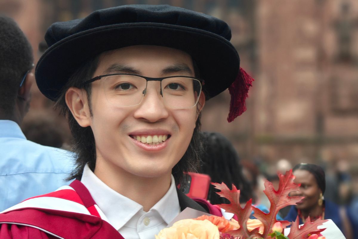 A head-and-shoulders photo of a man in a graduate cap and glasses smiling at the camera.