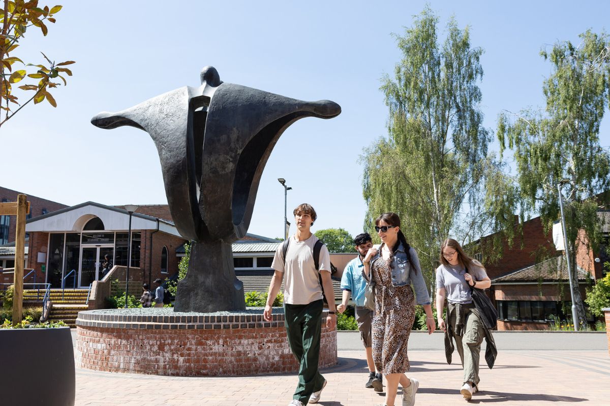 A group of students walking by a sculpture at the University of Chester Exton Park campus.