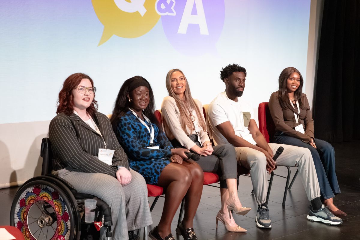 A group of people sitting in a row, looking off-camera. They are all smiling. In the background is a screen with a 'Q&A' graphic.
