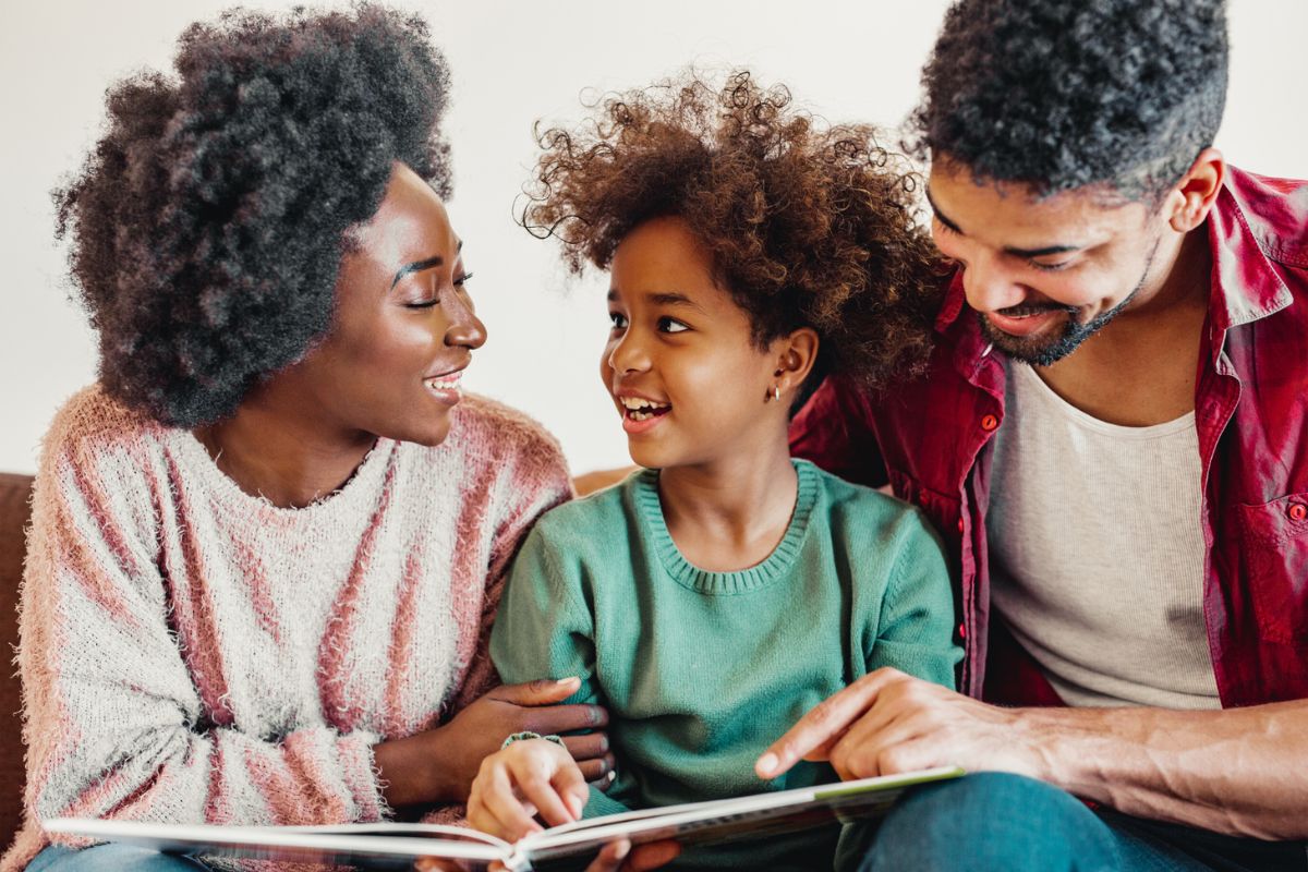 A staged family photo with two parents and a child looking at an open book. All three are smiling.