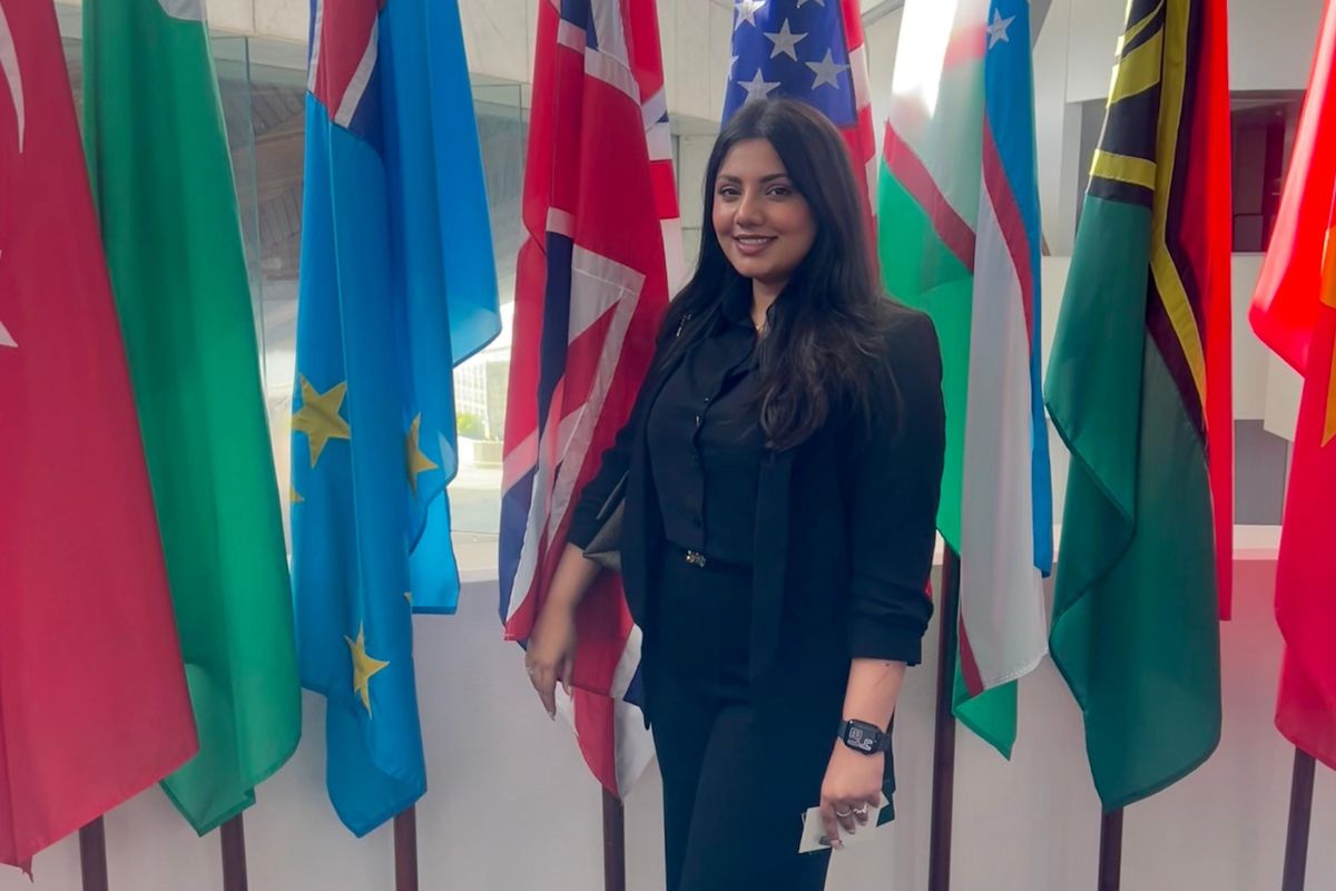 Noor Siddiqui standing in front of the flags of various countries.