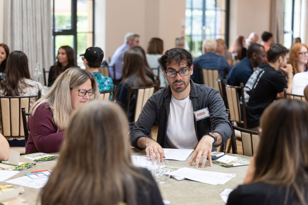 A number of round-table discussions in a busy room, with people talking to each other.