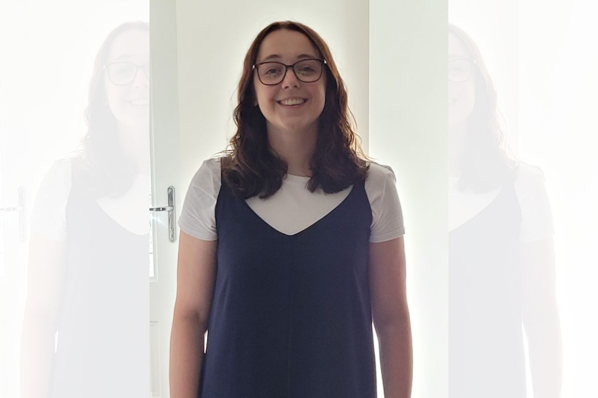 A woman in glasses standing and smiling at the camera.