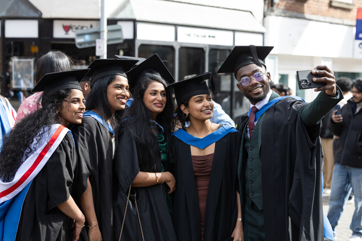A group of graduates in Chester city centre smiling and looking towards a phone for a selfie.