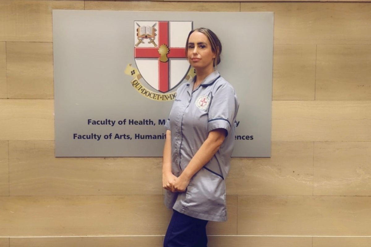 A picture of a woman in nursing uniform standing in front of a University of Chester sign