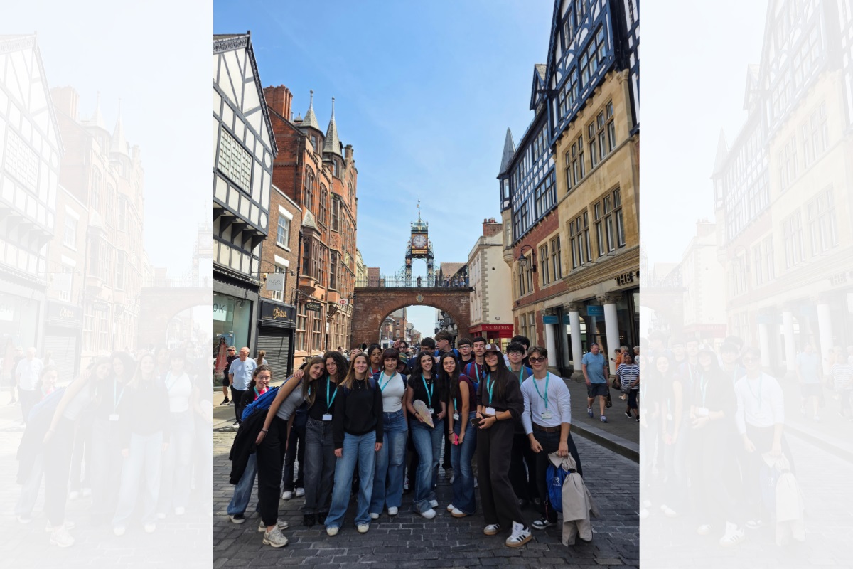 A group of students smiling and looking at the camera in Chester city centre on a clear day. In the background is the Eastgate Clock.