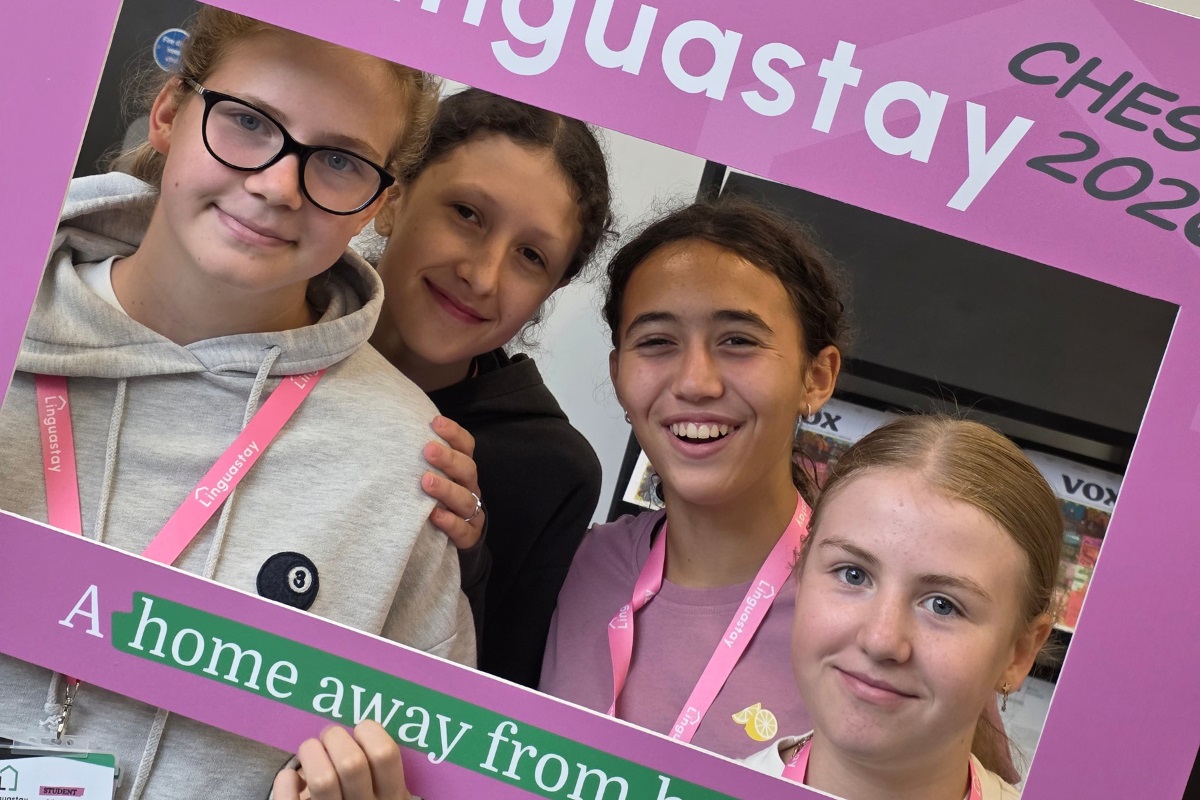 A group of four students smiling at the camera. They are holding up a framed promotional card which has the word 'Linguastay' on it.